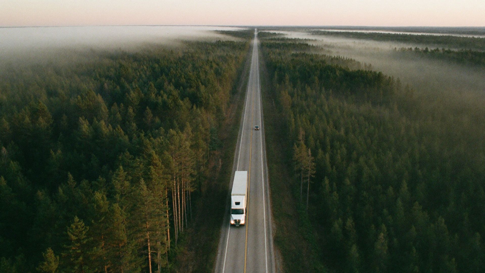 A transport truck on a highway through Canadian boreal forest at dawn