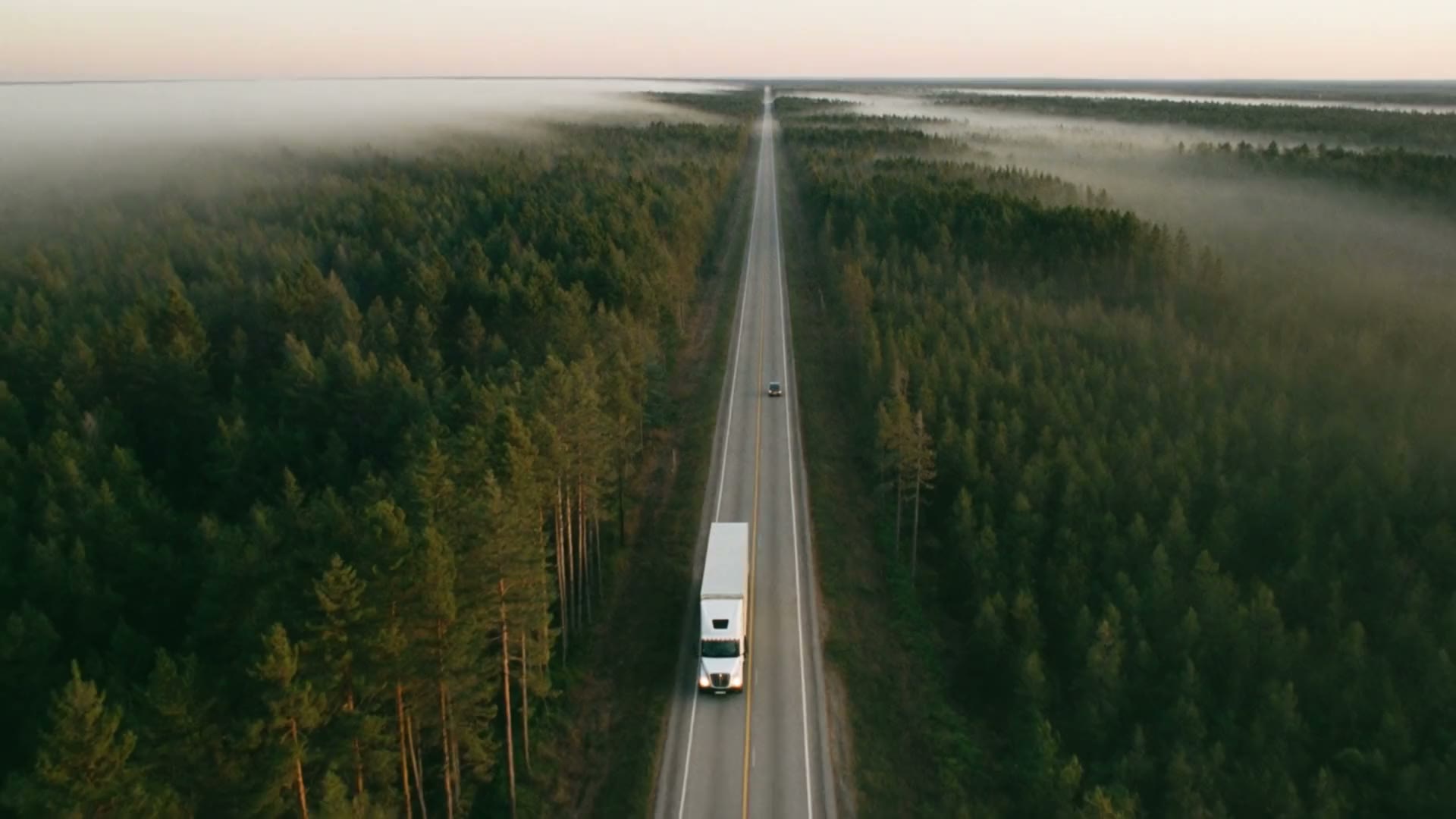 A transport truck on a dawn highway through Canadian boreal forest